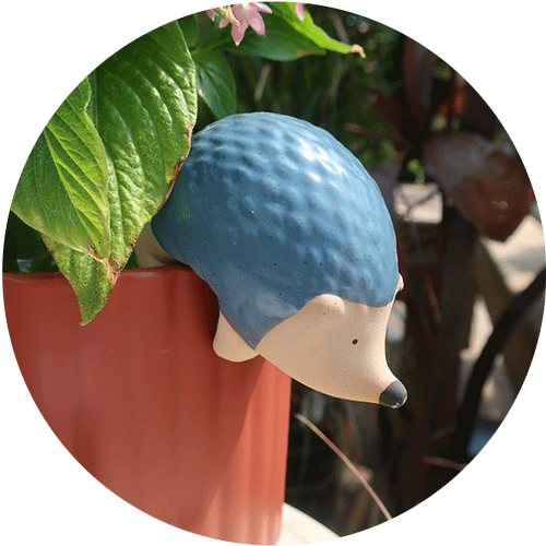 A small blue ceramic hedgehog hanging on the side of a rusty orange planter.